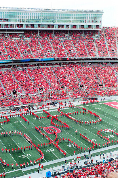 Packed stadium with sea of red shirts during pre-game field ceremony with marching formations.
