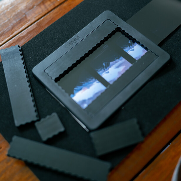 E-reader displaying two landscape photographs with sky and water, surrounded by dark protective cases on a wooden surface.