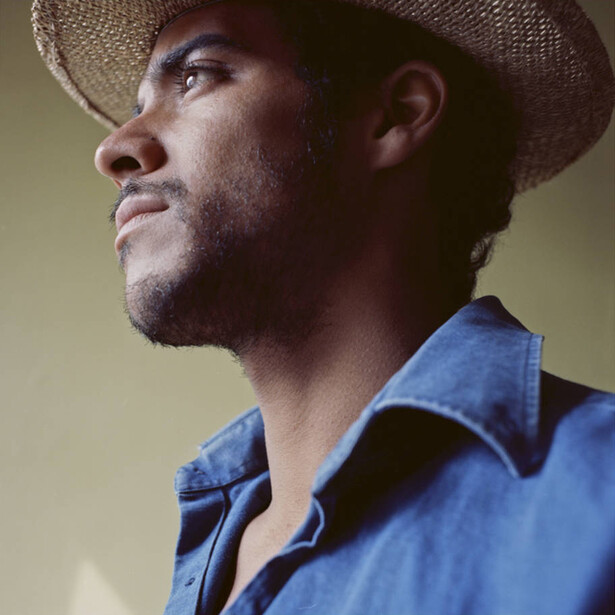 Man in denim shirt and cowboy hat looking upward in profile against warm background.