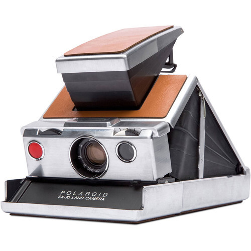 Vintage Polaroid SX-70 instant camera with wood-grain accents and brown leather strap displayed with flash unit and film cartridge.