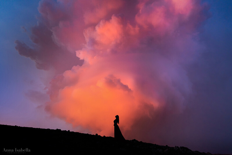 Silhouetted figure standing on a ridge against a dramatic sunset sky with vibrant orange and pink clouds.