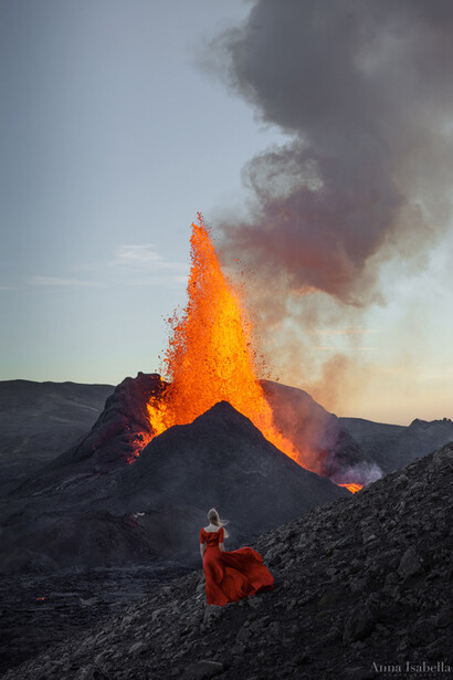 Lava fountain erupting from volcanic cone during golden hour, with thick smoke plume rising against clear sky.