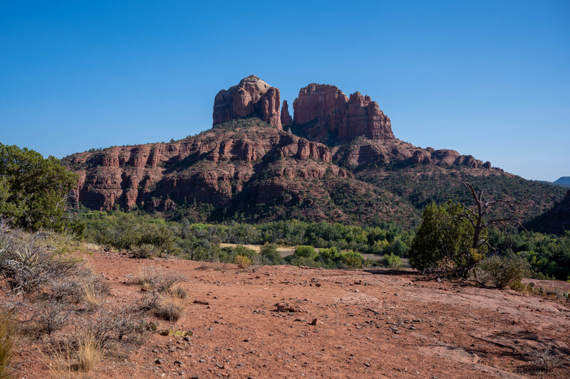 Twin red rock buttes rising from desert landscape with sparse vegetation under clear blue sky.