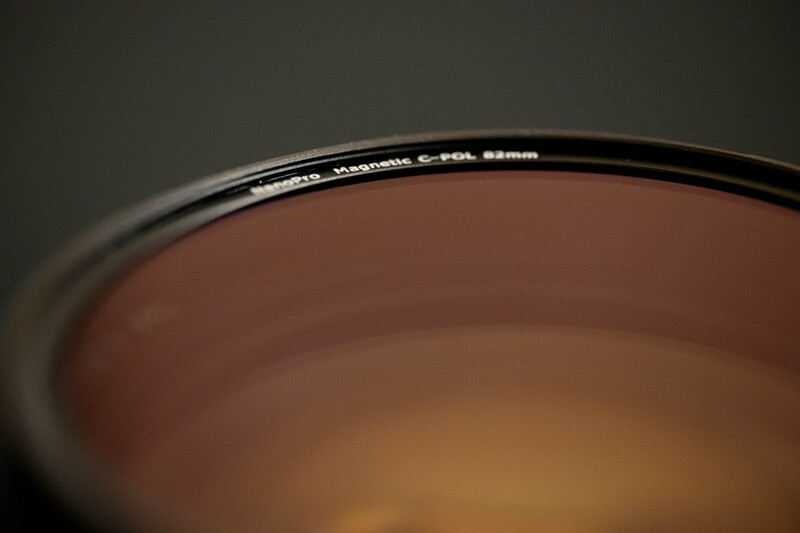 Close-up of a camera lens filter rim showing manufacturer markings and specifications against a blurred brown background.