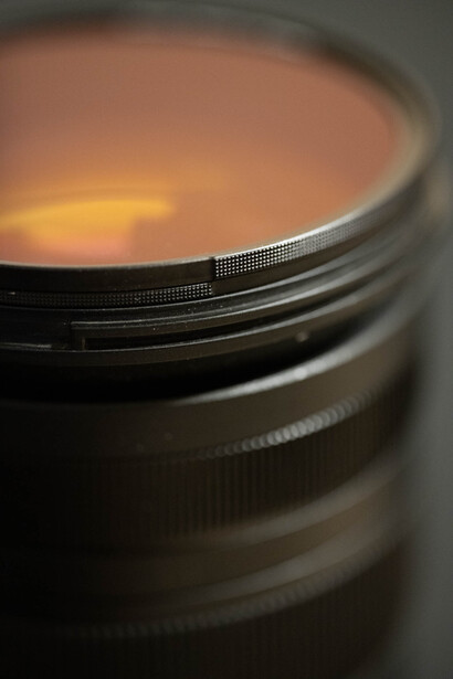 Close-up of a camera lens with warm golden and orange tones visible through the glass elements.