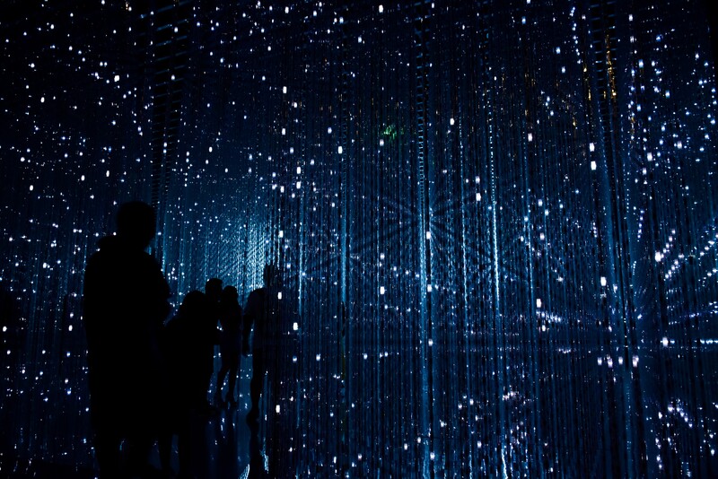 Silhouetted figures stand before an immersive digital display of cascading blue light particles and vertical data streams.