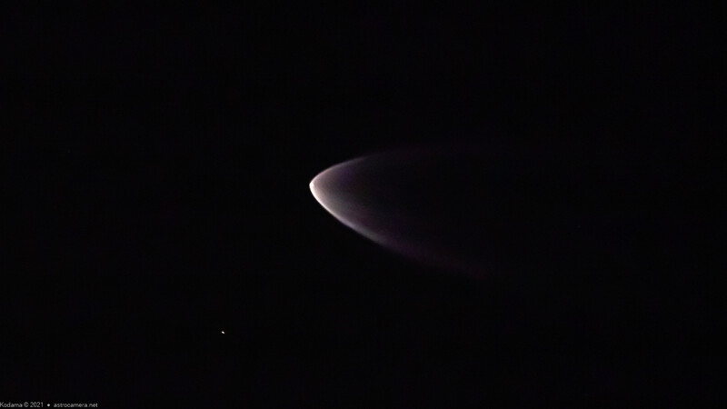Crescent-shaped luminous object against dark sky with subtle purple and white glow.