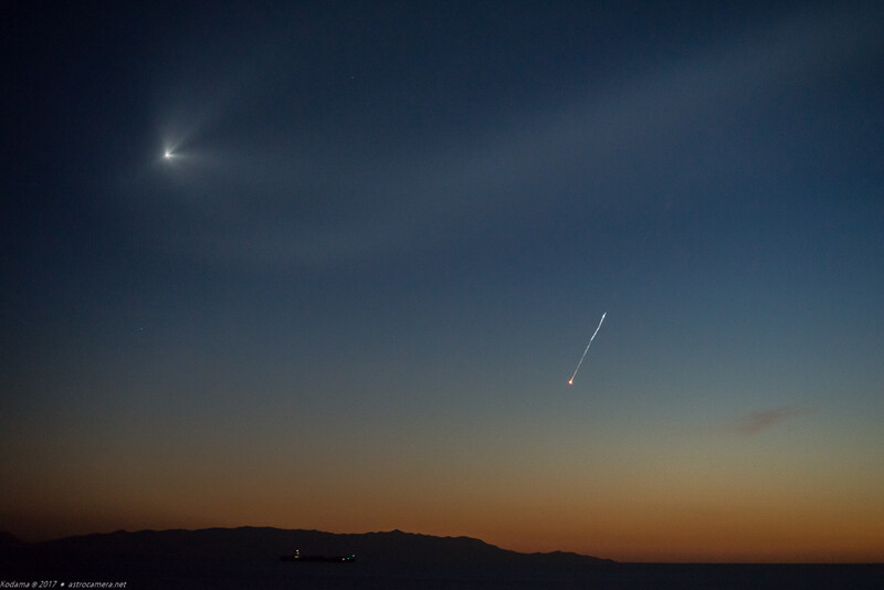 Twilight sky with bright celestial object on left and meteor or satellite streak on right above dark mountain silhouette.