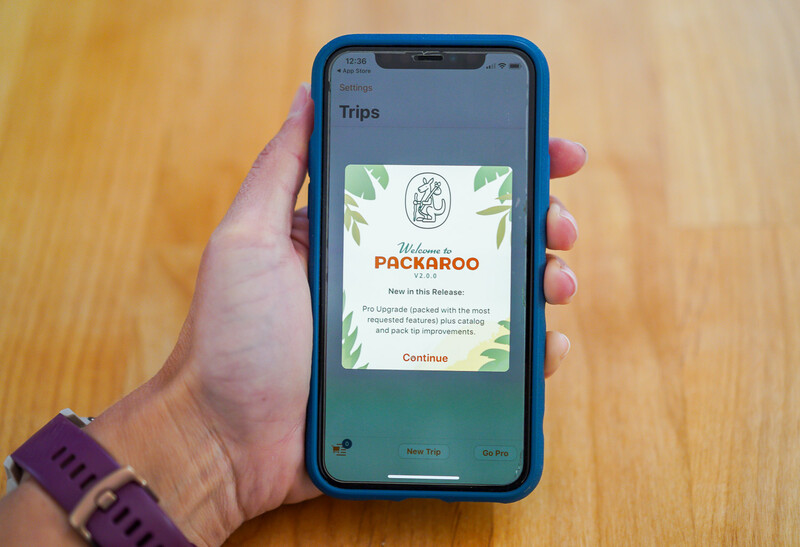 Screenshot of a travel app's Trips section displaying a Welcome to Packaroo card on a smartphone held in someone's hand.