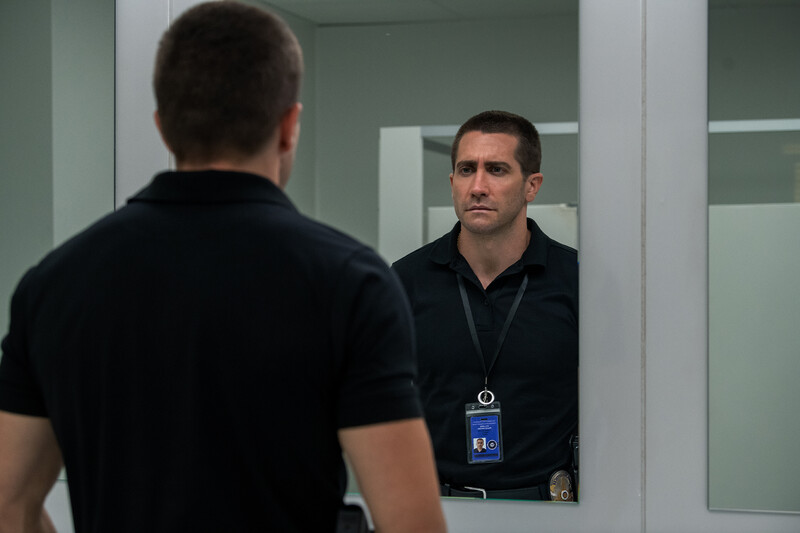 Man in dark shirt with ID badge looking at his reflection in a mirror.