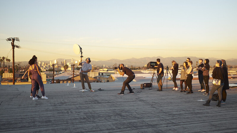 Group of people playing badminton on a rooftop with city skyline at sunset.