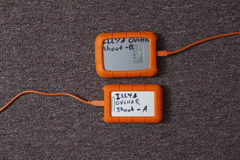 Two orange camera lens cases with handwritten labels lying on gray fabric with orange cables attached.