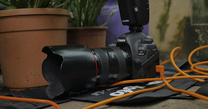 Canon EOS R5 Mark II camera with telephoto lens and external flash on orange cables in a studio setting.
