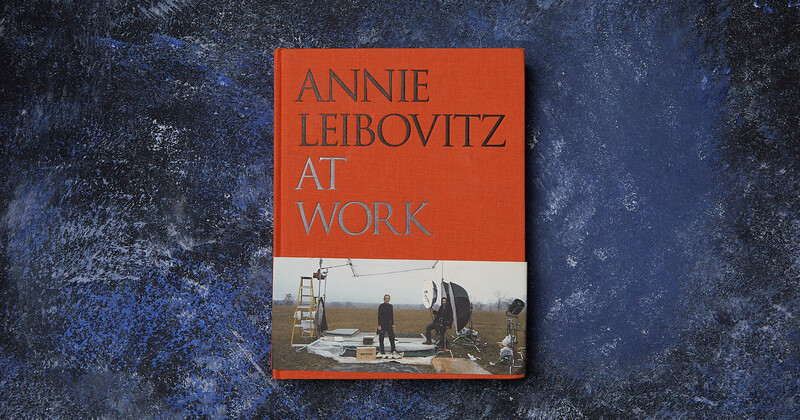 Book cover for 'Annie Leibovitz at Work' featuring an orange upper half with title text and a photograph of a photographer at work on set below.