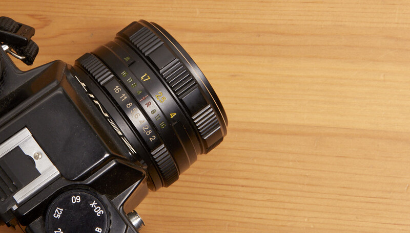Vintage SLR camera with manual focus lens mounted on wooden surface.