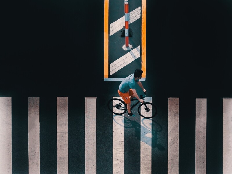 Overhead view of cyclist riding across white striped crosswalk with geometric shadow pattern.