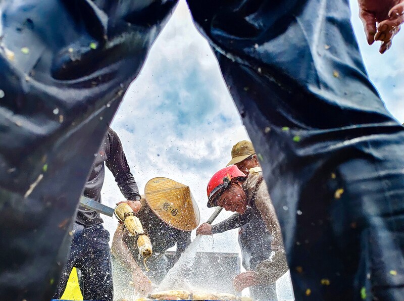 Construction workers gathered around materials in bright sunlight, shot from a low angle looking upward.