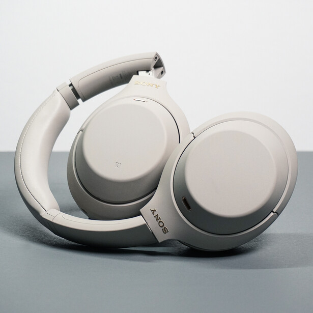 White over-ear headphones positioned on a gray surface with one ear cup folded up.