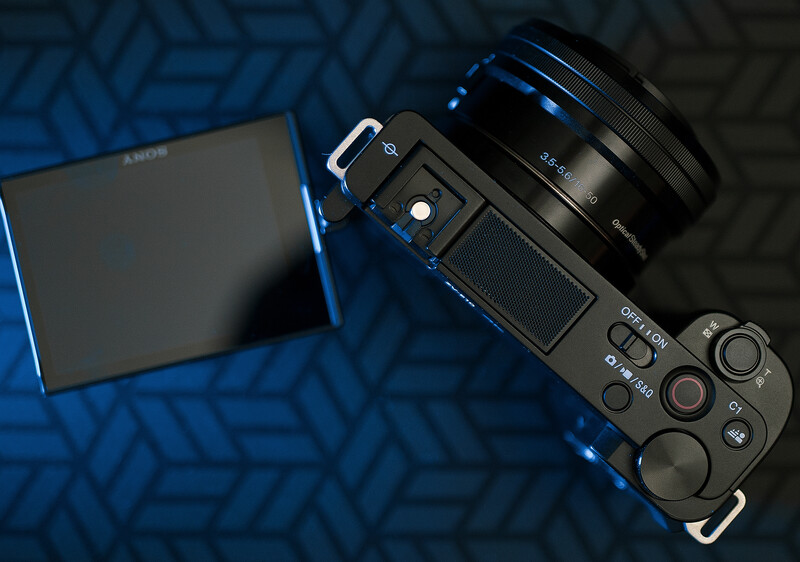 Sony mirrorless camera with attached lens on blue patterned surface next to open battery compartment.