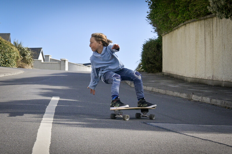 Young skateboarder in crouched position riding downhill on a residential street lined with concrete walls.