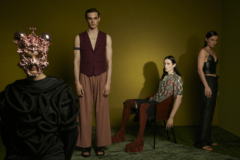 Four people posed in a studio against a yellow-green backdrop with dramatic shadows.