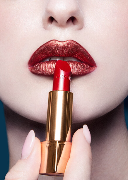 Close-up of a woman's lips wearing deep burgundy lipstick with a gold tube lipstick positioned in front.