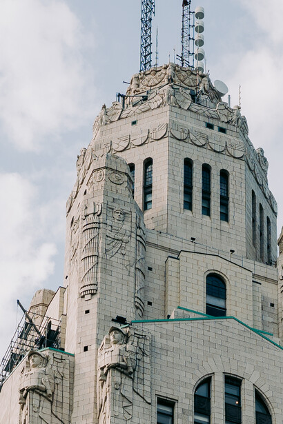 Art Deco building tower with white stone facade and ornamental details, antenna towers mounted on top.