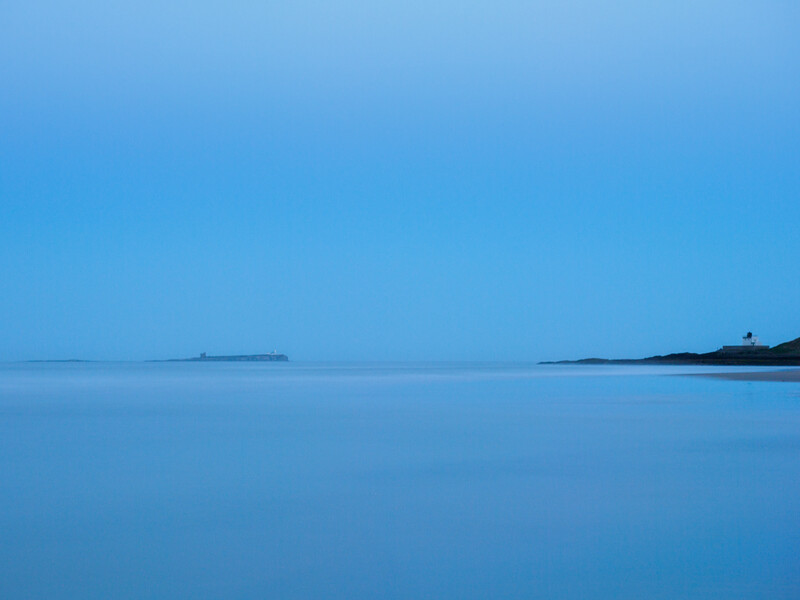 Minimalist seascape with calm water and distant landmasses under twilight sky.