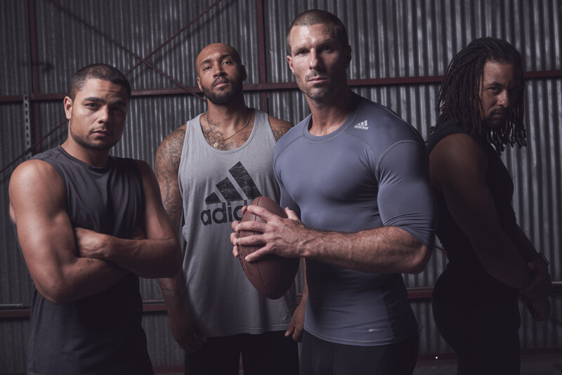 Four men posing together against a corrugated metal backdrop in studio lighting.