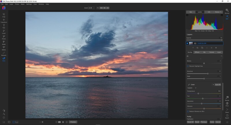 Dramatic sunset over calm ocean with vibrant orange, pink, and purple clouds reflected in water.