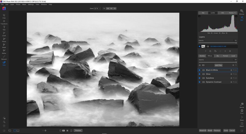 Long exposure seascape with dark rocks surrounded by smooth, milky white water against overcast sky.