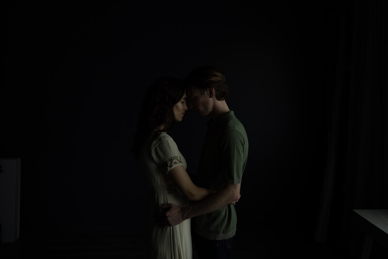 Two people embracing in profile against a dark background with dramatic side lighting.