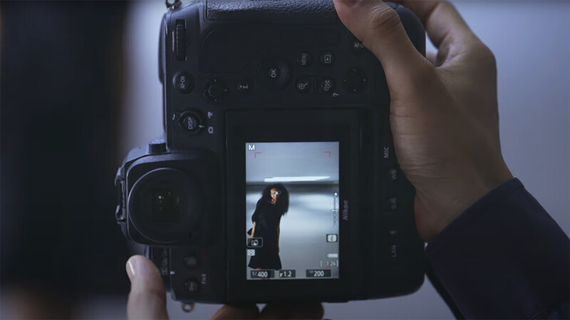 Photographer holding a digital camera with LCD screen displaying a portrait of a person against a bright window.