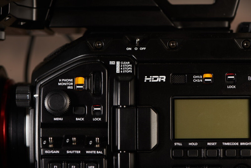 Close-up of professional video camera control panel showing buttons, switches, and LCD screen.