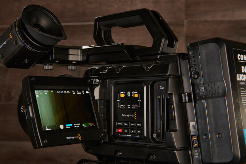 Professional cinema camera with articulating monitor and attached lens on wooden surface.