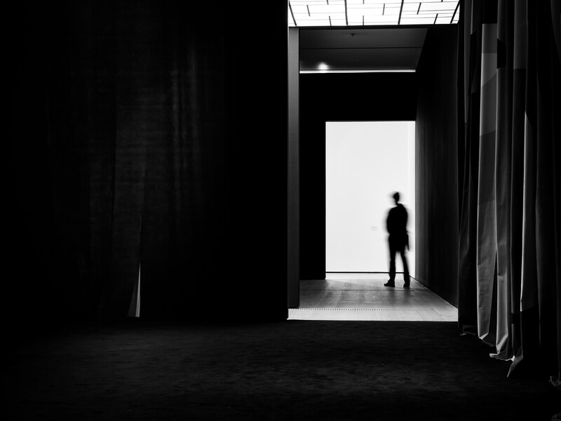 Silhouetted figure standing in a bright doorway within a dark architectural space.
