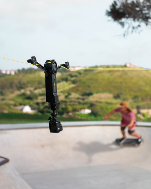 Electric scooter captured mid-air against a blurred hillside landscape with a rider visible in the background.
