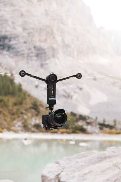 Drone hovering above a turquoise alpine lake with forested mountains in the background.