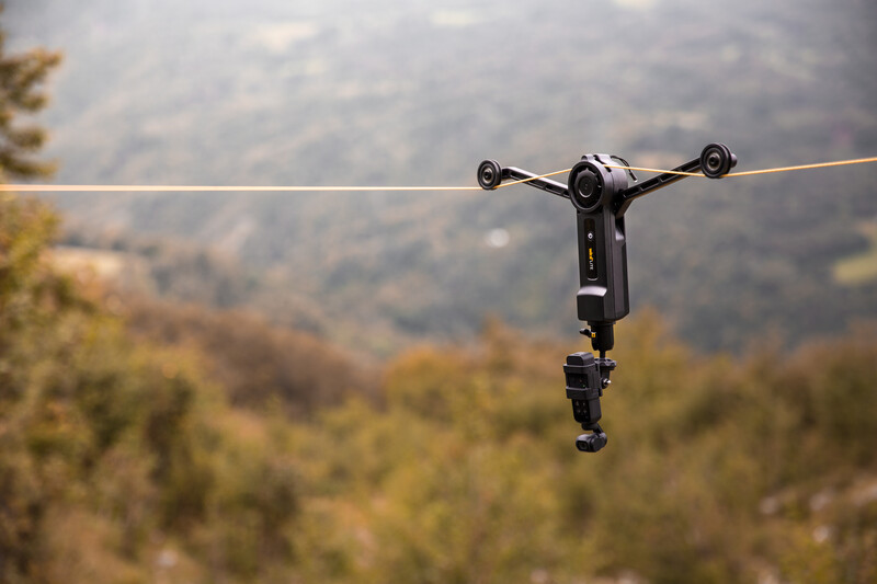 A zipline trolley hangs suspended on a cable with a forested valley visible in the soft-focused background.