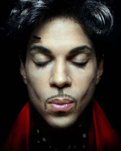 Portrait of a person with eyes closed against a black background, wearing a red garment.