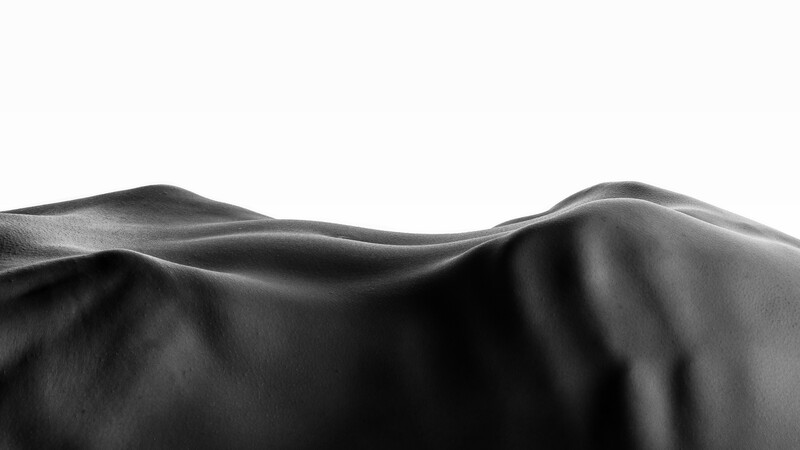 Smooth, undulating forms created by draped black fabric with dramatic directional lighting.