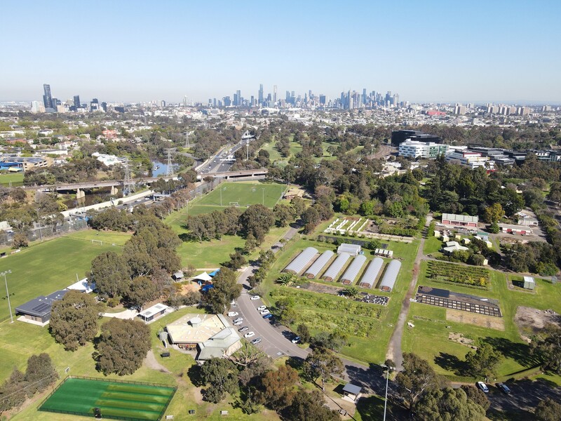Aerial view of a sports facility and parkland with a city skyline in the background.