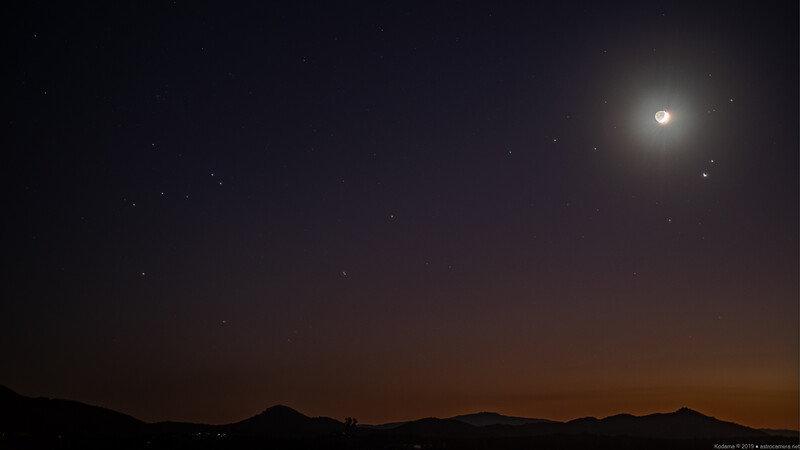 Moon rising above a dark mountain silhouette against a twilight sky with scattered stars.