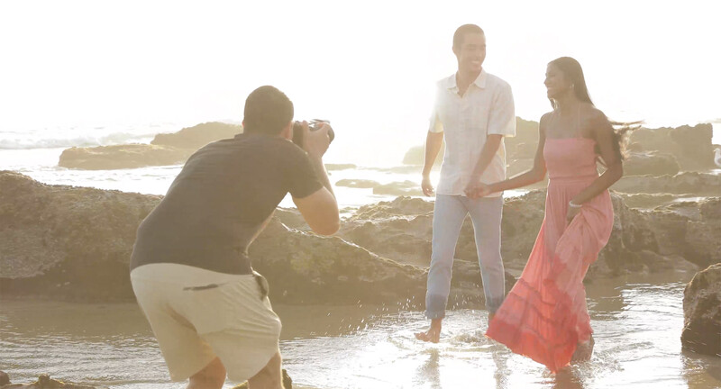 Photographer capturing a portrait of a couple standing in shallow water at golden hour.