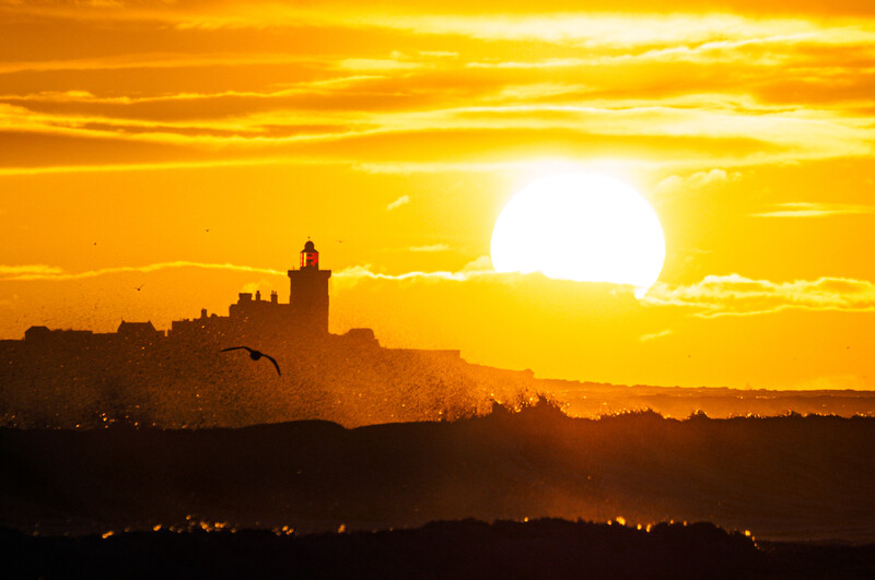 Silhouetted castle or fortified structure on a hilltop against a massive golden sunset sun.
