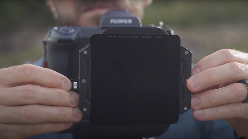 Photographer holding a large format camera filter or dark slide in both hands during outdoor shooting.