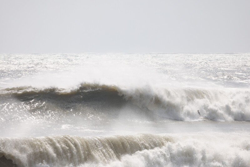 Powerful ocean waves with white spray crashing against each other under overcast sky.