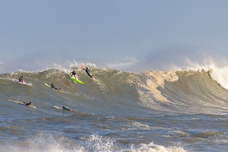 Multiple surfers riding a large wave with dramatic lighting and spray.