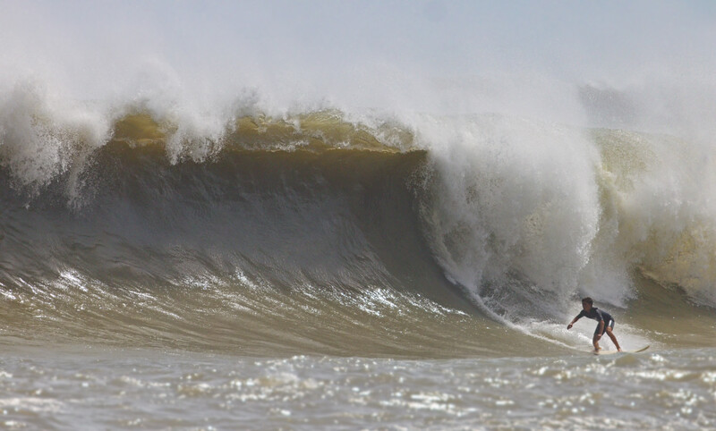 Surfer riding a massive wave with dramatic spray and foam crashing over the crest.