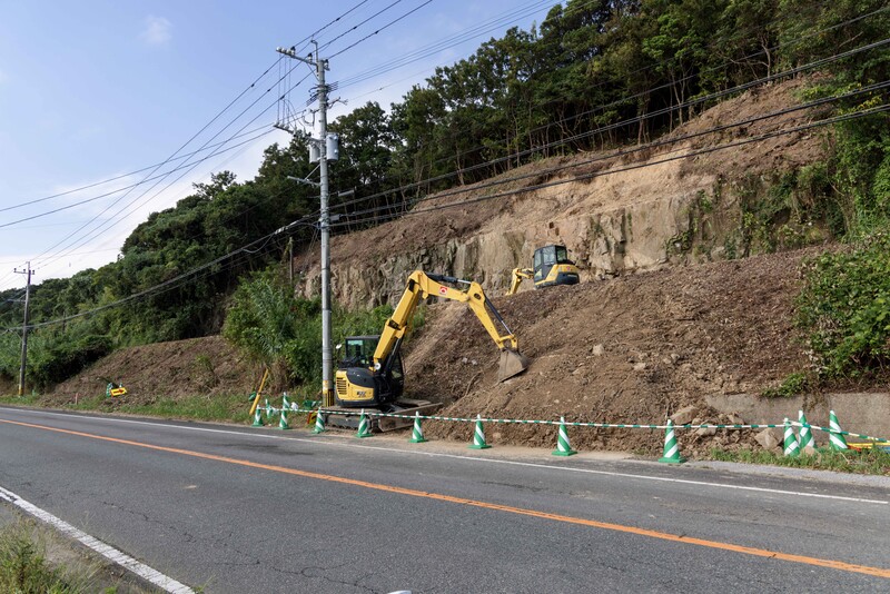 Yellow excavator working on exposed hillside earth during road construction under clear sky.